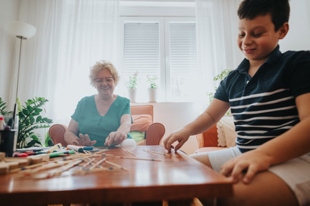 Young boy playing pick-up sticks with grandmother in cozy living roomの写真素材