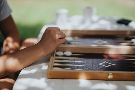 Close-up of a hand playing a backgammon game outdoors on a sunny day, evoking relaxation and leisure...
