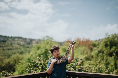 Young girl joyfully playing with pet snake outdoors on a sunny dayの写真素材