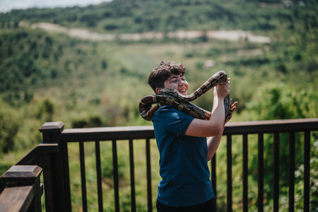 Girl joyfully interacts with pet snakes on sunny outdoor deckの写真素材