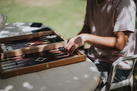 Person playing an engaging game of backgammon outdoors, enjoying a peaceful afternoon under the shade. Focused on strategy and leisure in a natural setting during a sunny day.の写真素材