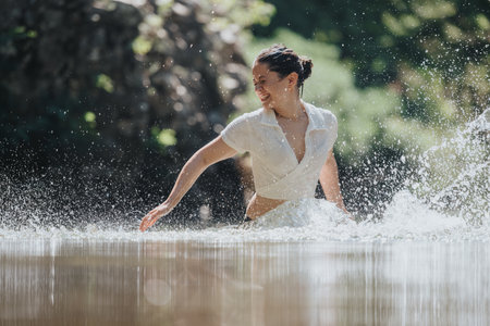 Joyful woman splashing water in scenic natural settingの写真素材