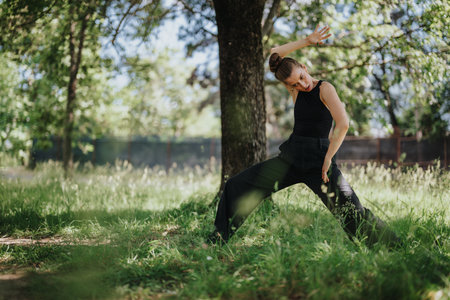 Lovely girl dancing in nature, performing modern dance movements in a lush green parkの写真素材