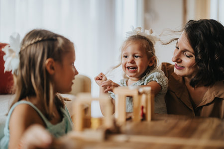 Happy mom playing with her daughters at home with wooden blocks