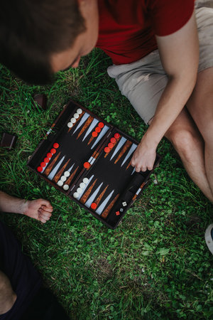 Two friends enjoying a game of backgammon outdoors on the grass