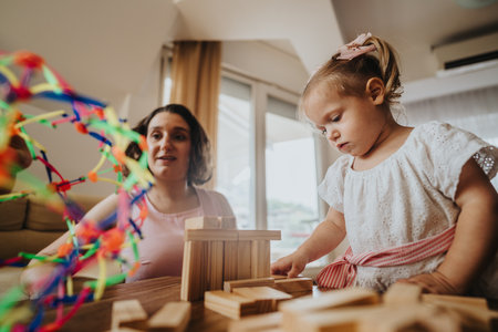 Mother and daughter playing with wooden blocks and colorful toys indoors on a cozy dayの写真素材