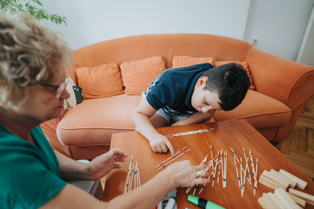 Young boy playing pick-up sticks with grandmother in cozy living roomの写真素材