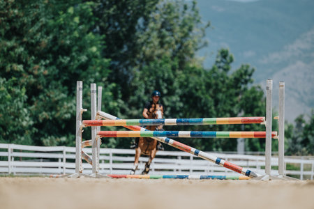 Equestrian rider approaching colorful obstacle in outdoor arena with mountains in backgroundの写真素材