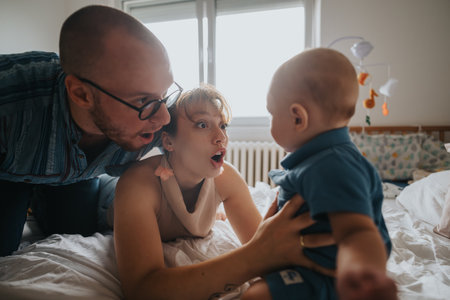 Surprised parents engaging with baby in a cozy bedroom settingの写真素材