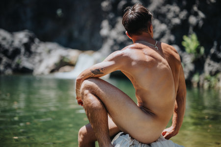 Young man enjoying the natural beauty of an outdoor waterfall and serene lake in the summerの写真素材