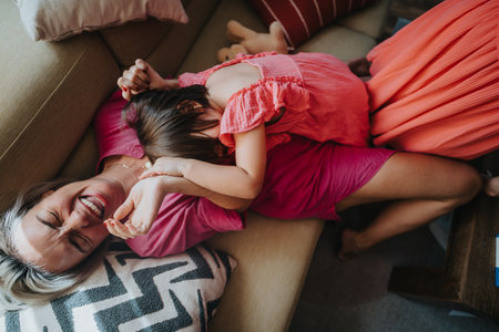 Joyful family moment of mother and daughter laughing on the couchの写真素材