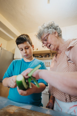 Grandmother teaching young boy to peel cucumber in cozy kitchenの写真素材