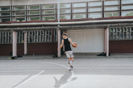 Young friends enjoy playing basketball on an old neighborhood court under the sun, showcasing teamwork and fun.の写真素材