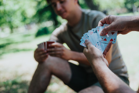 Friends playing a card game outdoors on a sunny dayの写真素材
