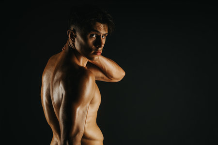 Muscular shirtless man posing confidently in a dark studio settingの写真素材