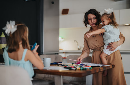 Mother helping daughters with craft activities in the kitchenの写真素材