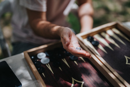 Persons hand holding dice over a backgammon board during an outdoor game session conveying leisure and strategy.の写真素材