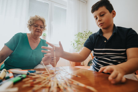 Young boy playing pick-up sticks with grandmother at homeの写真素材