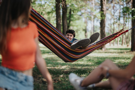 Group of friends relaxing in a colorful hammock in a forest setting on a sunny dayの写真素材