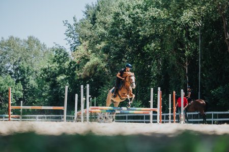 Equestrian jumping over obstacle during outdoor competition on a bright sunny dayの写真素材