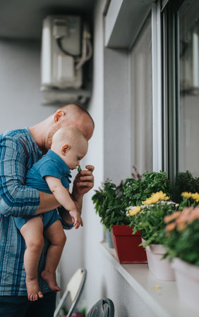 Father and baby bonding over fragrant flowers on balconyの写真素材