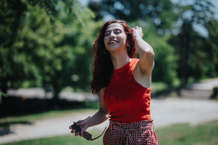 Happy woman enjoying a sunny day in the park with friends, wearing red top and checkered skirtの写真素材