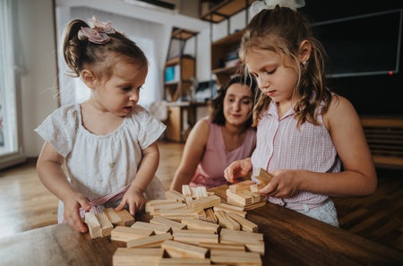 Two young sisters enjoying family time building with wooden blocks indoorsの写真素材