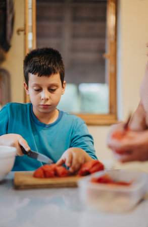 Young boy slicing strawberries in a cozy kitchen settingの写真素材
