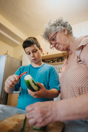 Grandmother teaching her grandson to peel in the kitchenの写真素材