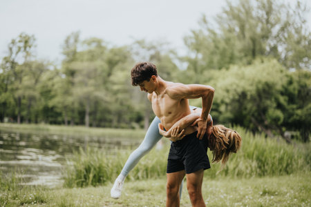Fit young couple performing acrobatic exercise routine in nature parkの写真素材