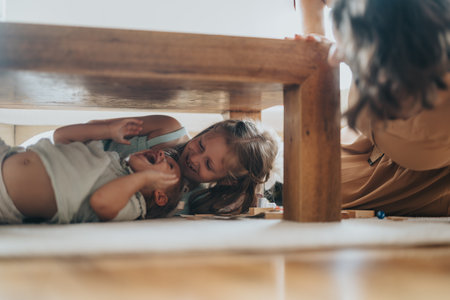 Children playing joyfully under a wooden table at homeの写真素材