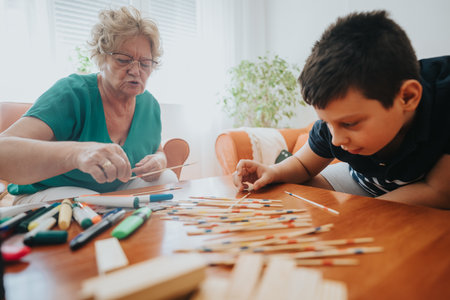 Young boy playing pick-up sticks with grandmother in cozy living roomの写真素材