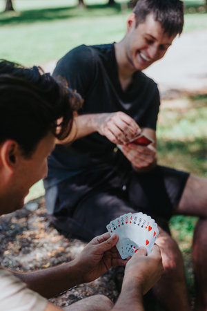 Two friends enjoying playing cards outdoors in a sunny parkの写真素材