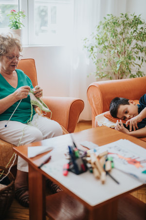 Young boy enjoys phone while grandmother knits in cozy living roomの写真素材