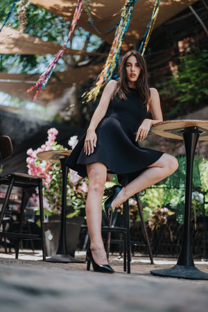 Gorgeous woman posing elegantly in outdoor cafe wearing a black dressの写真素材