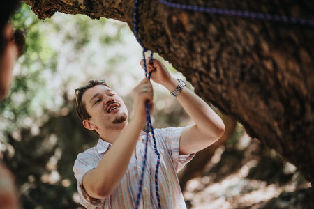 Man tying rope on tree branch during outdoor adventure activityの写真素材