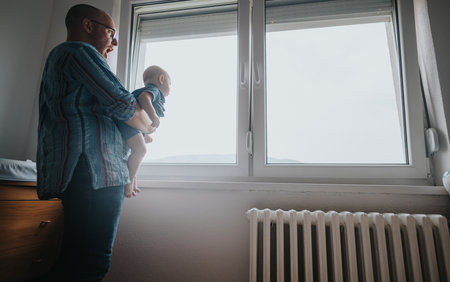 Father holding baby gazing out the window on a peaceful morningの写真素材