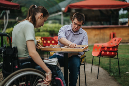 Boy with Down syndrome and girl in wheelchair playing backgammon outsideの写真素材