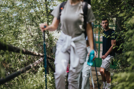 Group hiking through a lush green forest with walking sticks on a sunny dayの写真素材