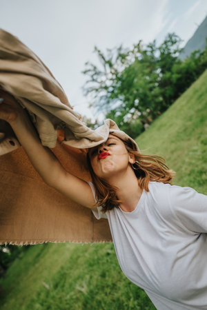 Joyful woman playing in the park with blanket on a windy dayの写真素材