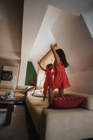 Joyful sisters jumping on the couch in a cozy living roomの写真素材