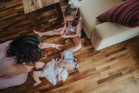 Mother playing with her daughters on the wooden floor of the living roomの写真素材