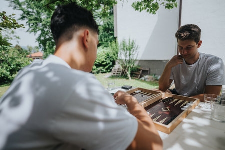 Friends playing backgammon outdoors on a sunny day in the gardenの写真素材