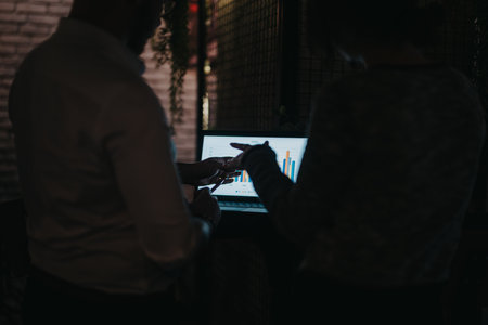 Business colleagues analyzing data on a laptop during a discussion in a dimly lit officeの写真素材