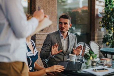 Business meeting in an outdoor cafe setting with professionals discussing plans and strategies over coffee and laptopsの写真素材