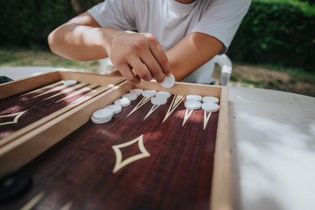 Man playing backgammon outdoors on a sunny day with focus on boardの写真素材