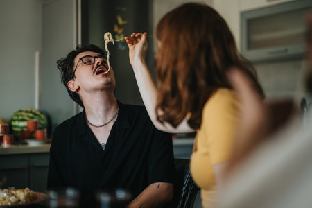 Playful couple sharing spaghetti in cozy kitchen settingの写真素材