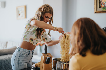 Young woman serving pasta to friends at home dinnerの写真素材