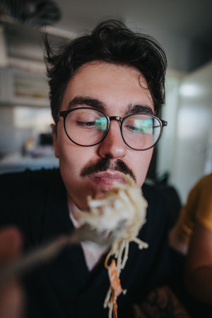 Man wearing glasses enjoying a delicious pasta meal at homeの写真素材