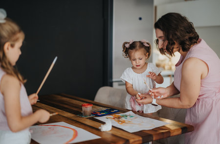 Young mother drawing and painting with her little daughters at homeの写真素材